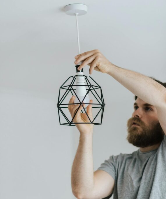 Concentrated repairman screwing light bulb in stylish lamp hanging on ceiling of new flat