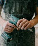 Crop anonymous mechanic in uniform with wireless drill standing in flat during repair works